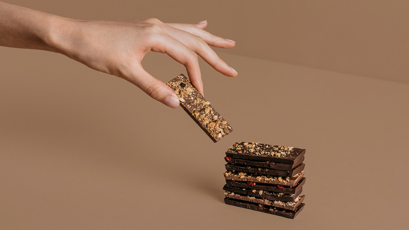 Una mano de forma delicada coge unos trozos de chocolate partidos y apilados