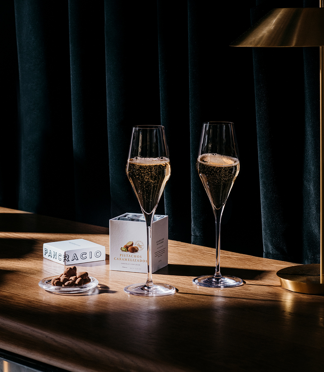 Dos copas de champagne junto a chocolates Pancracio con una luz suave y sombras