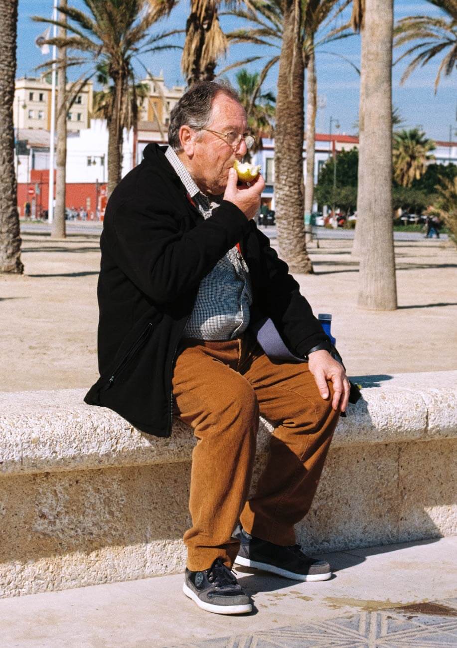 Un señor se come una manzana en el paseo marítimo sentado en el muro