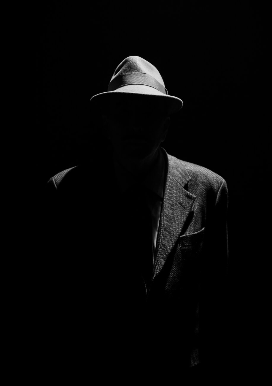 Foto muy oscurecida de una persona con chaqueta y sombrero a la que no se le ve la cara