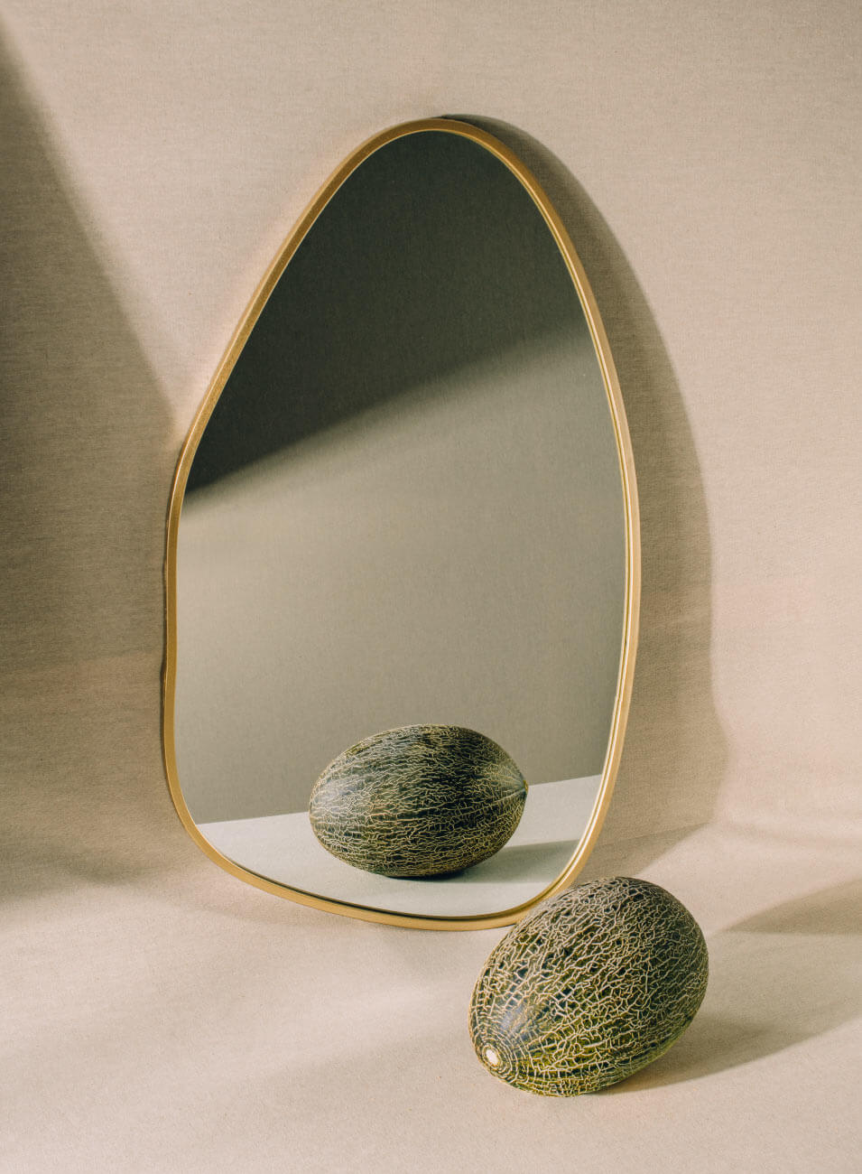 Un melón fotografiado delante de un espejo de marco dorado y forma redondeada irregular