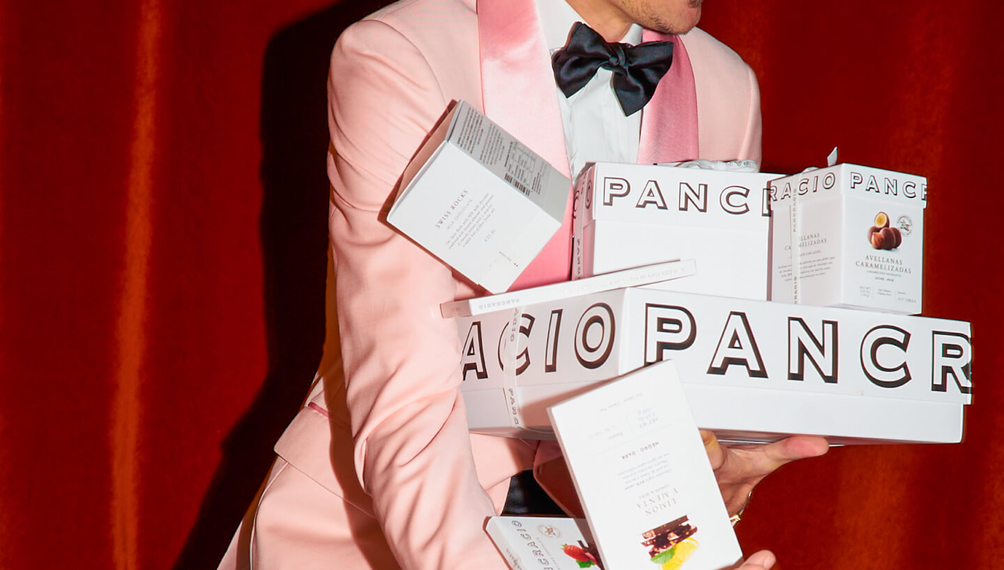Hombre con chaqueta rosa y pajarita sostiene varios paquetes de Chocolates Pancracio