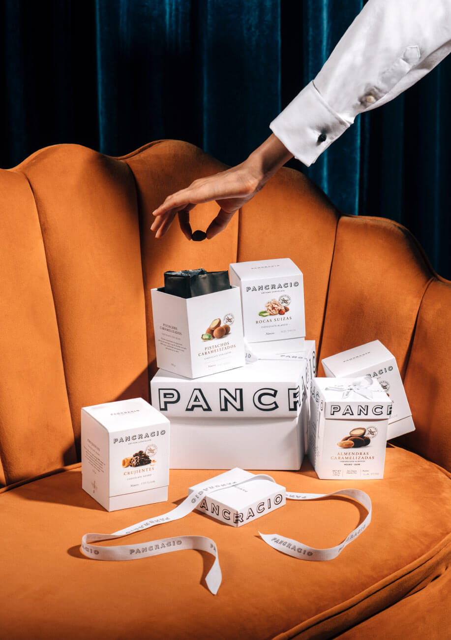 Una mano coge un chocolate de unas cajas sobre un sofá de color naranja